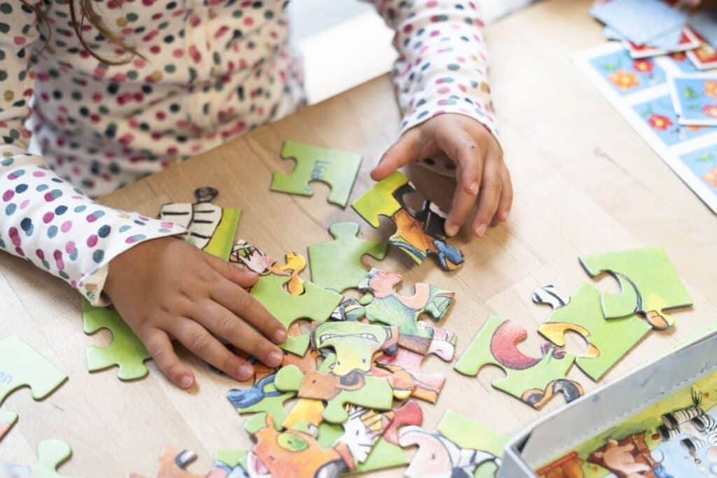 Ein Kind mit einem gepunkteten Shirt setzt bunte Puzzleteile auf einem Holztisch zusammen.