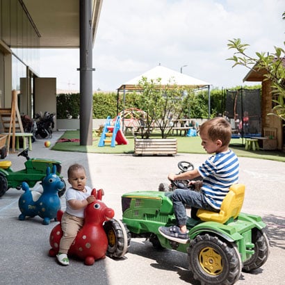 Zwei Kinder auf Spielzeug-Traktor und-Lauffigur im Garten der Kinderkrippe miKaDo